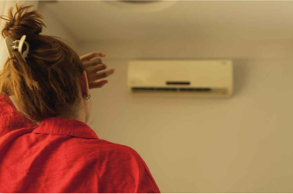 A young girl standing in front of air conditioner to chill out in a hot summer day.